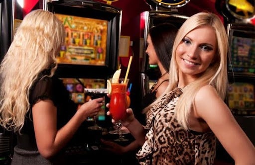 Three girls holding drinks in their hand while hanging around slot machines