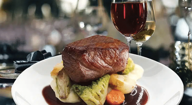 Nicely cooked filet mignon over a stack of cooked vegetables paired with glasses of wine
